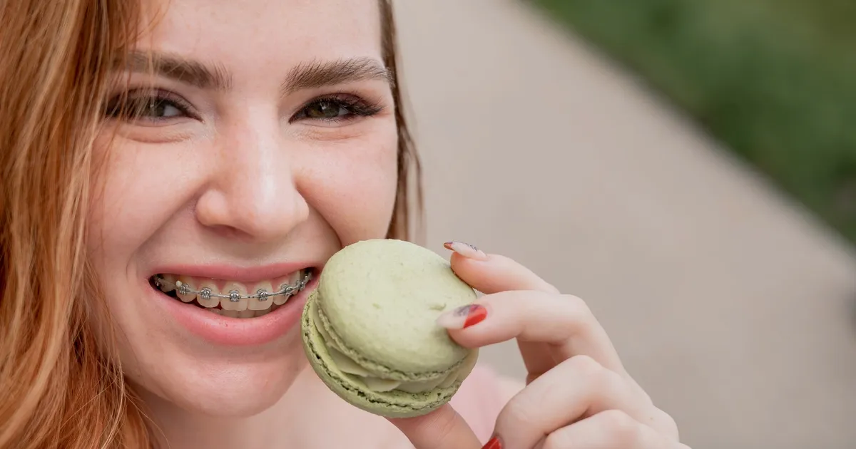 Dziewczyna z aparatem na zębach gryząca zielonego makaronika