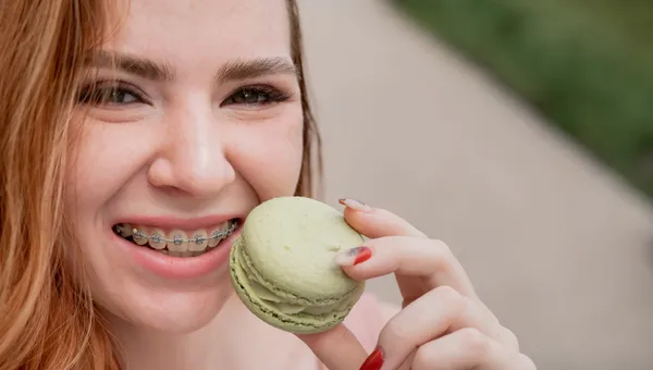 Dziewczyna z aparatem na zębach gryząca zielonego makaronika
