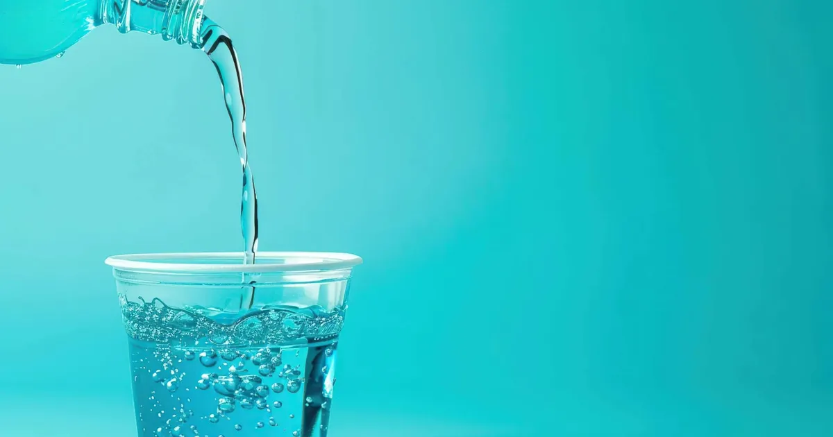 Niebieski płyn do płukania jamy ustnej wlewany do plastikowego kubeczka
