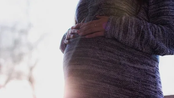Kobieta w ciąży trzymająca dłonie na brzuchu w promieniach słońca