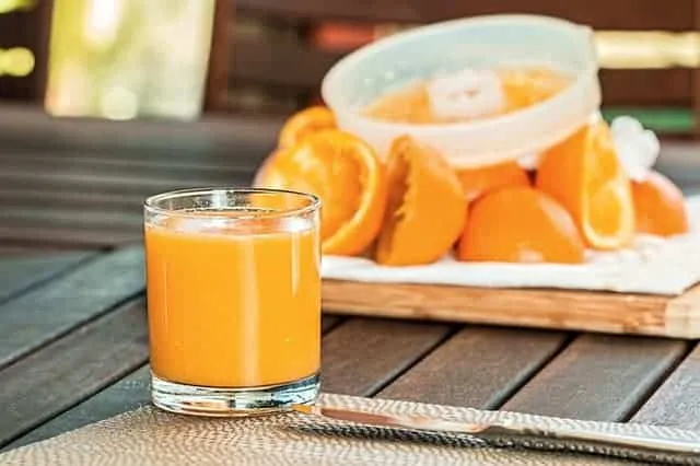 Szklanka soku pomarańczowego obok wyciskarki i przekrojonych pomarańczy